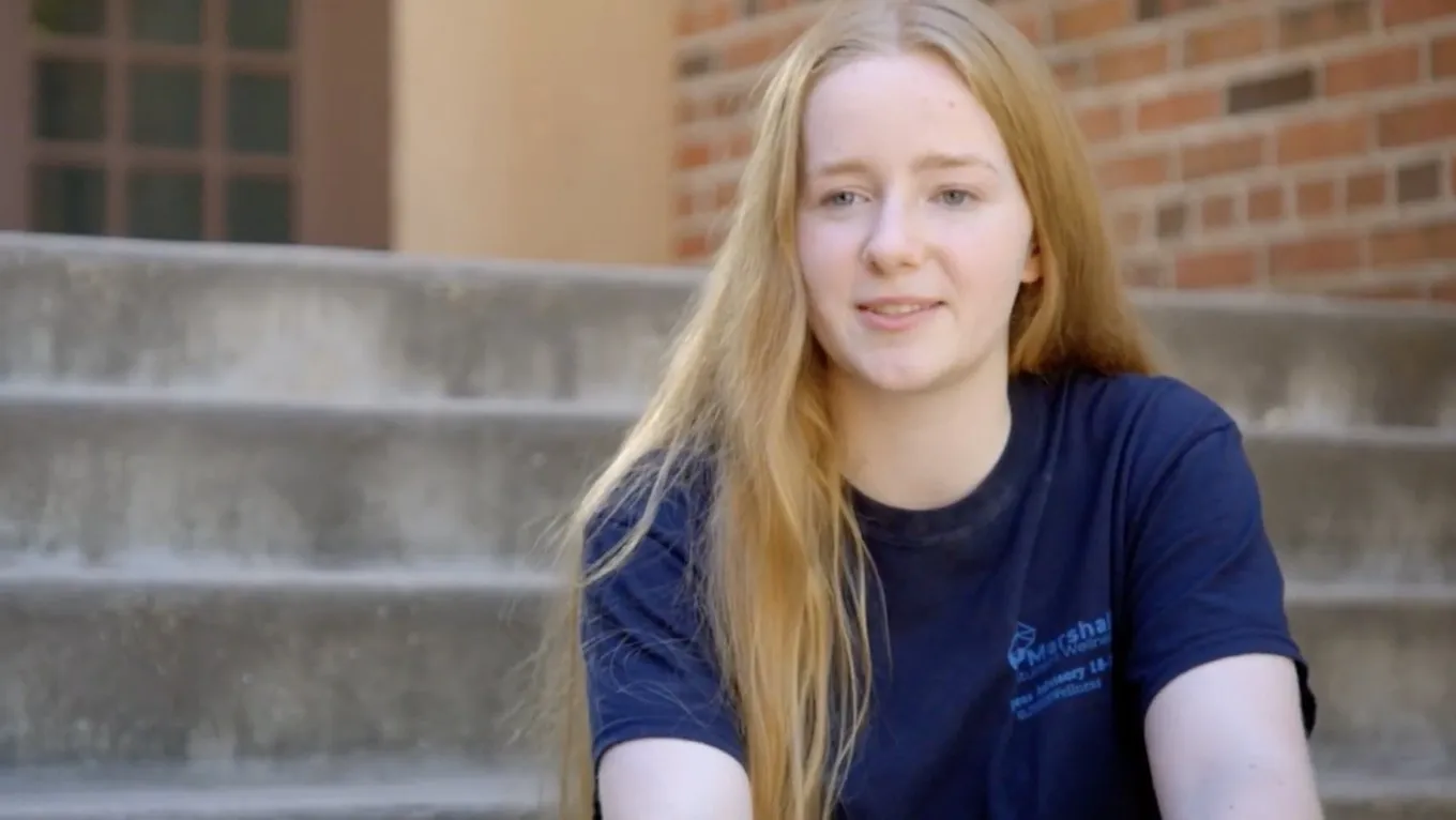 A high school student in a Wellness Advisory shirt sits on the school steps