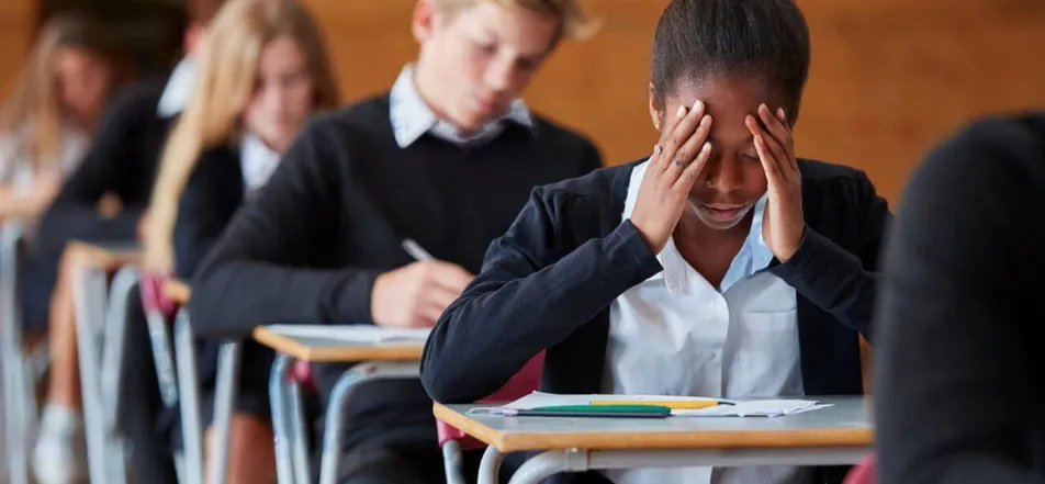 A student holds her head in her hands during an exam while classmates write
