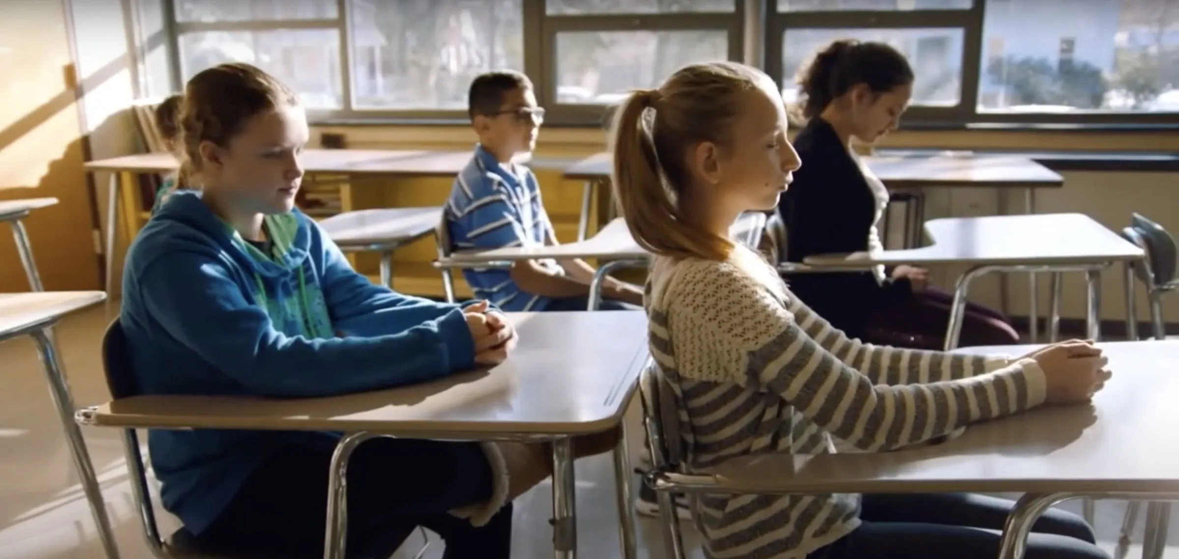 Middle school students sit upright at their desks with eyes closed during a daily mindfulness practice