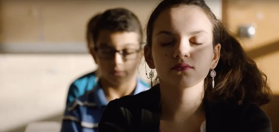 A student sits with eyes closed in a sunlit classroom during a daily mindfulness practice