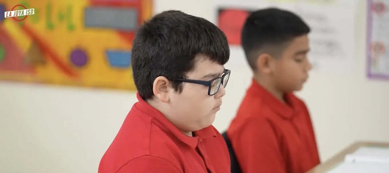 Two students in red shirts sit quietly at their desks during a mindfulness practice