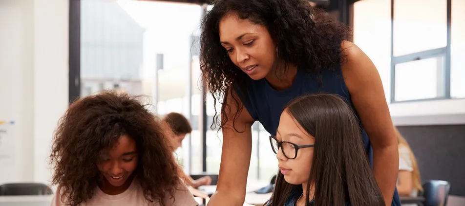 A teacher leans in to help two students at their desks
